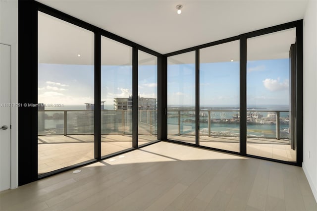 spare room with light wood-type flooring, a water view, and expansive windows