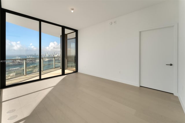 spare room featuring expansive windows, light wood-type flooring, a water view, and plenty of natural light