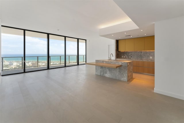 kitchen featuring floor to ceiling windows, backsplash, a center island with sink, a water view, and a view of the beach