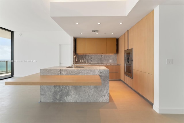 kitchen with light brown cabinetry, tasteful backsplash, expansive windows, stainless steel double oven, and sink