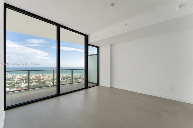 unfurnished room with plenty of natural light, expansive windows, a water view, and a beach view