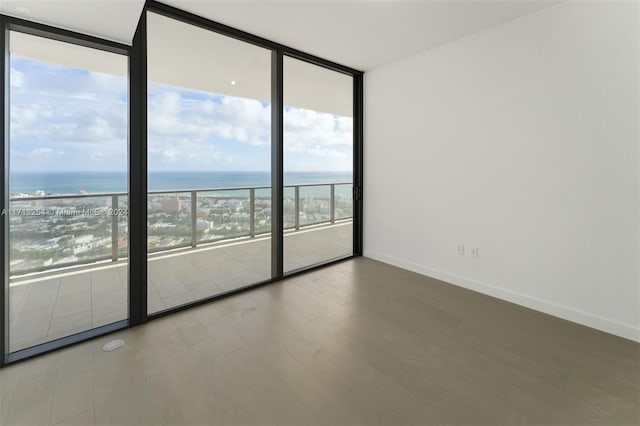 empty room featuring plenty of natural light, a water view, a beach view, and a wall of windows