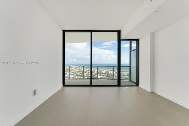 spare room with expansive windows, a water view, and light hardwood / wood-style floors