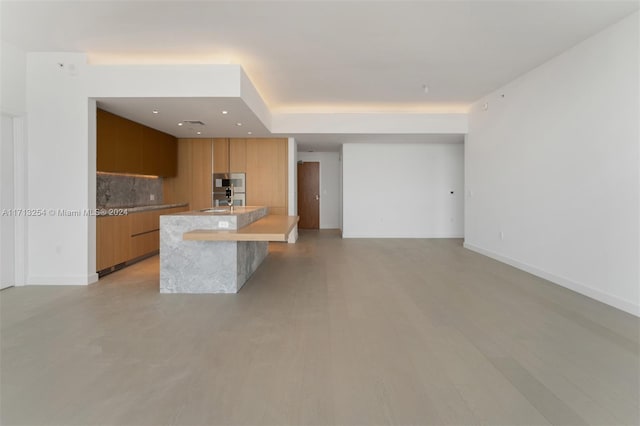 kitchen with a breakfast bar, decorative backsplash, sink, and an island with sink