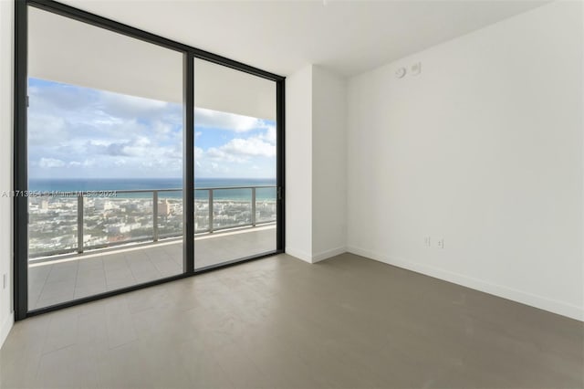 spare room with a view of the beach, a water view, plenty of natural light, and floor to ceiling windows