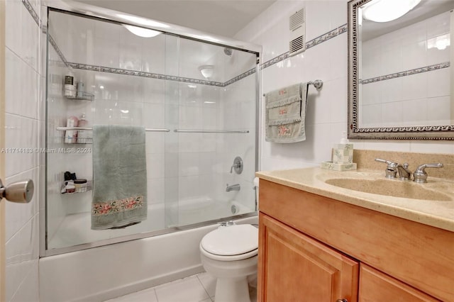 full bathroom featuring tile patterned flooring, toilet, shower / bath combination with glass door, vanity, and tile walls