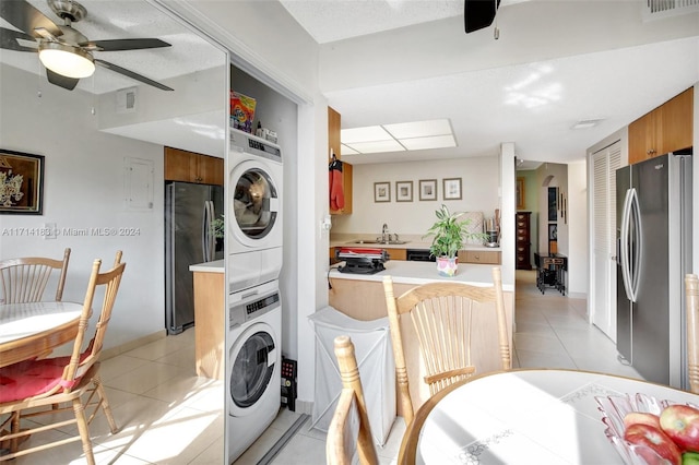 laundry room featuring light tile patterned floors, stacked washer and dryer, ceiling fan, and sink