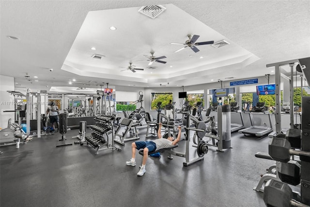 workout area with a textured ceiling, a tray ceiling, and ceiling fan