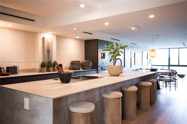 kitchen featuring black electric stovetop, a center island, a kitchen bar, expansive windows, and dark wood-type flooring