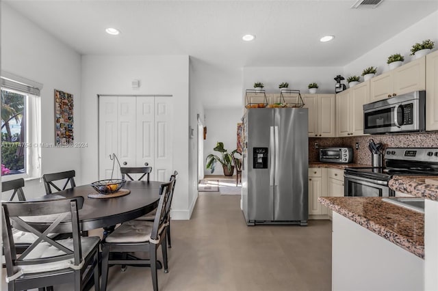 kitchen with dark stone counters, tasteful backsplash, cream cabinetry, and appliances with stainless steel finishes