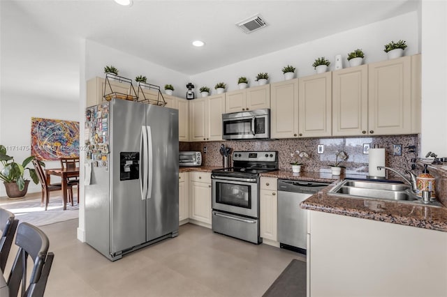 kitchen with sink, dark stone countertops, cream cabinetry, decorative backsplash, and appliances with stainless steel finishes