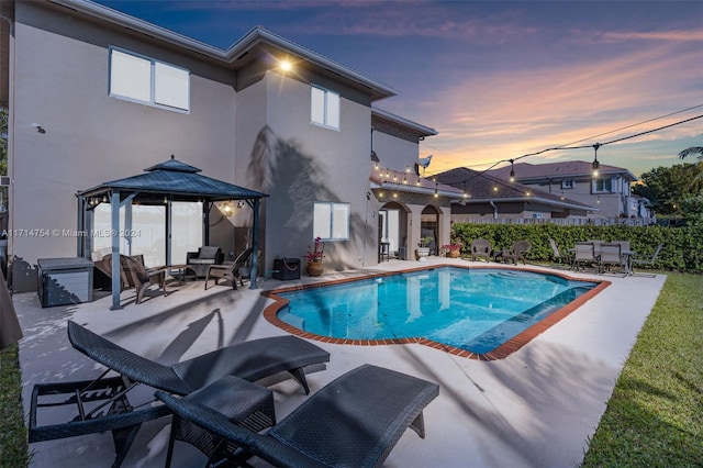 pool at dusk featuring a gazebo and a patio area