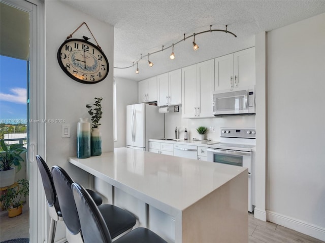 kitchen with white appliances, kitchen peninsula, a textured ceiling, white cabinetry, and a breakfast bar area