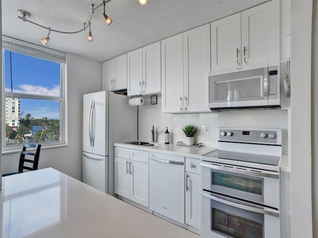 kitchen featuring sink, a textured ceiling, track lighting, white appliances, and white cabinets