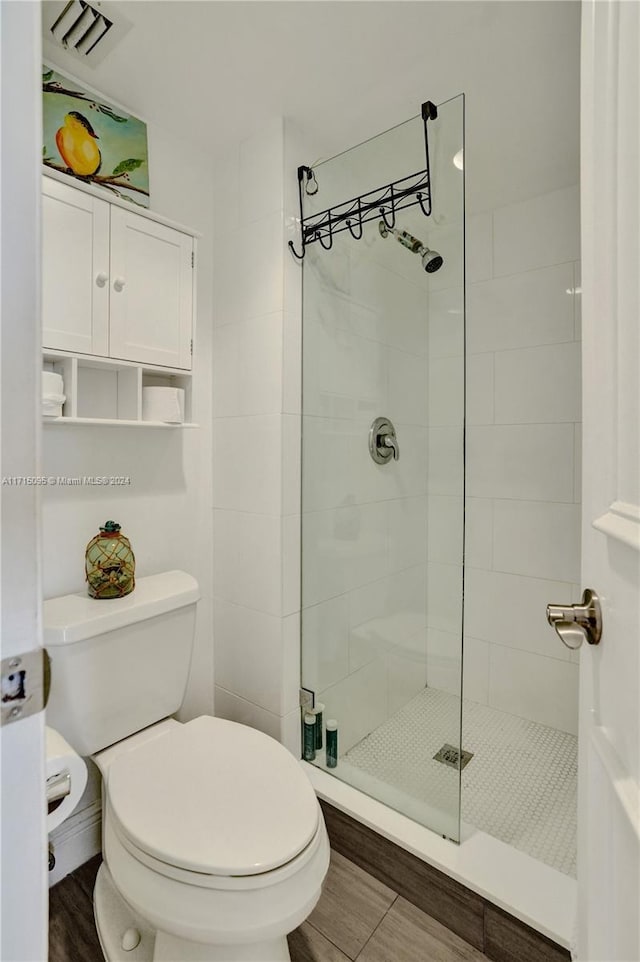 bathroom with tiled shower, wood-type flooring, and toilet