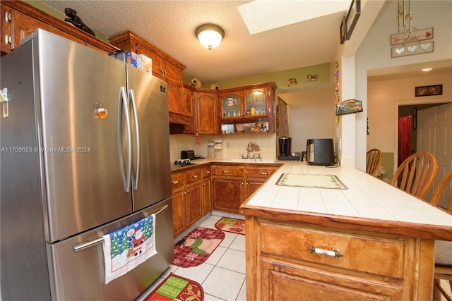 kitchen with decorative backsplash, stainless steel fridge, tile counters, a kitchen bar, and kitchen peninsula