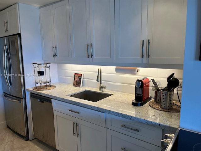 kitchen featuring white cabinets, light stone counters, stainless steel appliances, and a sink