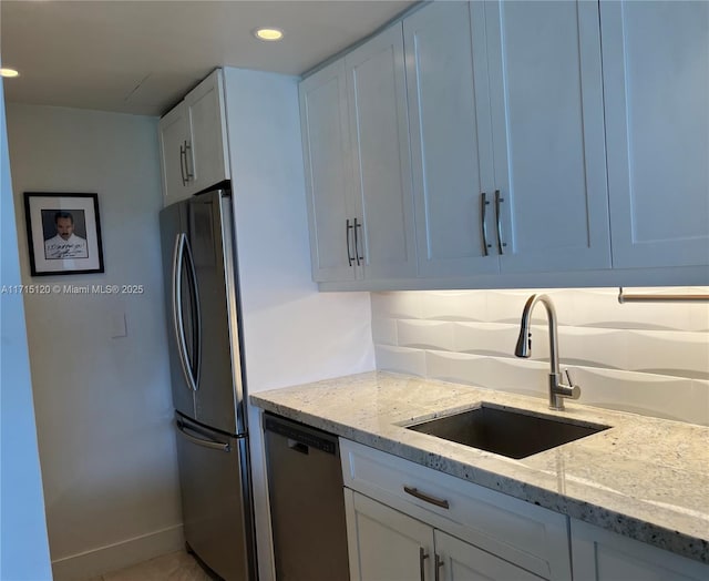 kitchen with a sink, appliances with stainless steel finishes, light stone counters, and white cabinetry