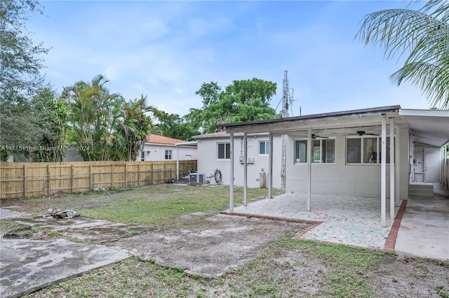 rear view of property featuring a carport, cooling unit, ceiling fan, a yard, and a patio