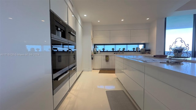 kitchen with oven, white cabinetry, and sink