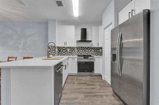 kitchen with kitchen peninsula, a breakfast bar, stainless steel appliances, sink, and wall chimney range hood