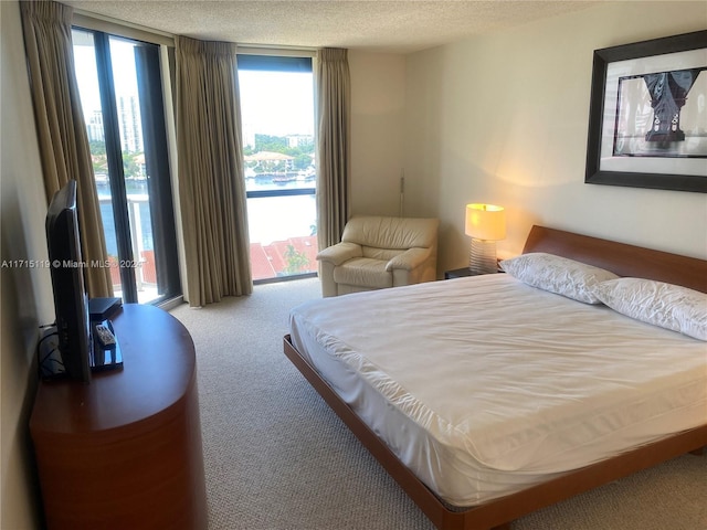 bedroom featuring carpet flooring, a wall of windows, a textured ceiling, and access to outside