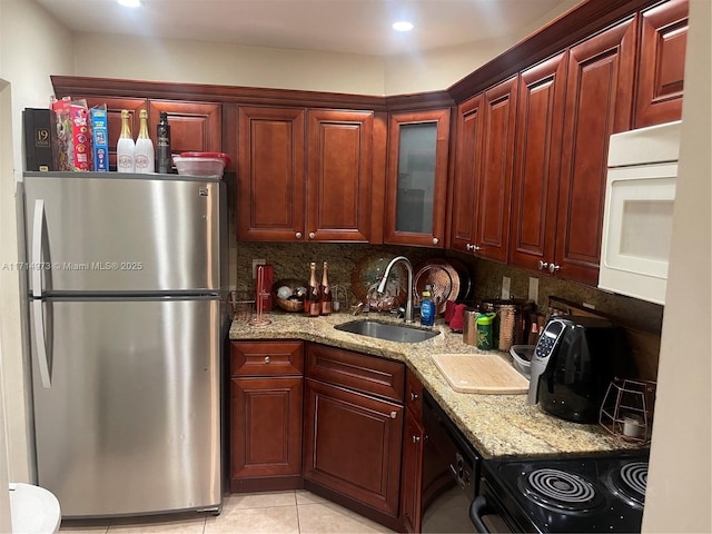 kitchen featuring stove, backsplash, sink, stainless steel fridge, and light stone counters