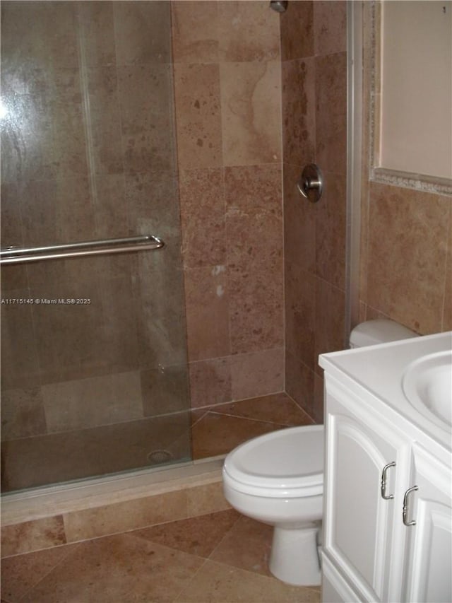 bathroom featuring tile patterned floors, vanity, tiled shower, tile walls, and toilet