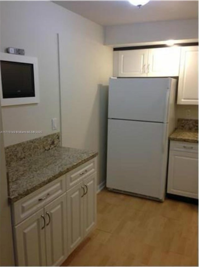 kitchen featuring white cabinets, light stone countertops, white fridge, and light wood-type flooring