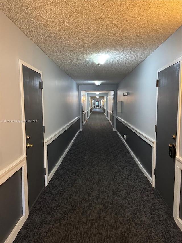 hall featuring a textured ceiling and dark carpet