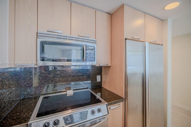 kitchen with decorative backsplash, dark stone countertops, light brown cabinetry, and appliances with stainless steel finishes