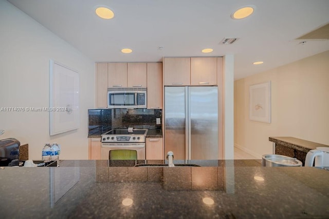 kitchen with decorative backsplash, light brown cabinetry, stainless steel appliances, and dark stone countertops