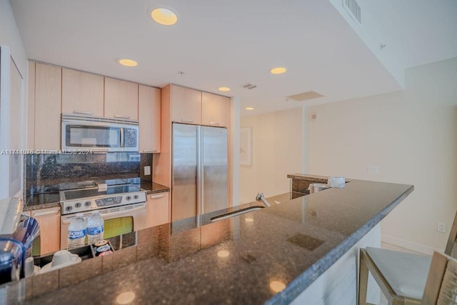 kitchen featuring light brown cabinetry, backsplash, stainless steel appliances, sink, and dark stone countertops