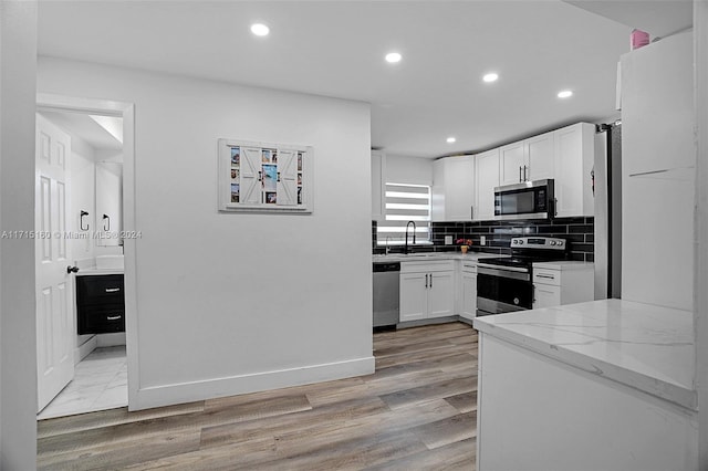 kitchen with white cabinetry, light stone countertops, tasteful backsplash, appliances with stainless steel finishes, and light wood-type flooring