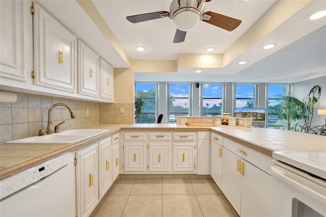 kitchen with backsplash, white dishwasher, white cabinets, sink, and tile counters