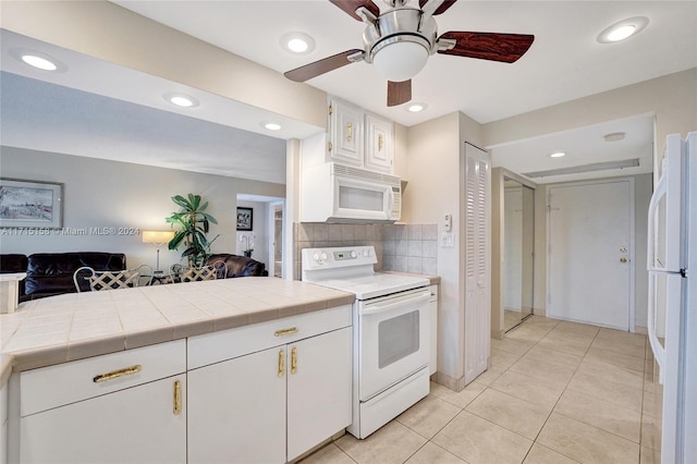 kitchen featuring white appliances, backsplash, tile counters, light tile patterned flooring, and white cabinetry