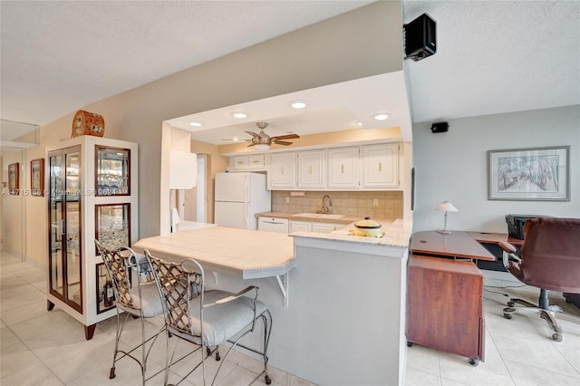 kitchen featuring backsplash, sink, light tile patterned floors, white fridge, and kitchen peninsula