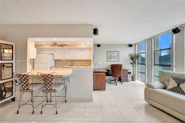 kitchen featuring kitchen peninsula, decorative backsplash, a kitchen bar, sink, and white fridge