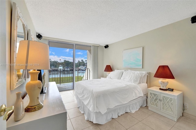 tiled bedroom featuring expansive windows, access to exterior, a textured ceiling, and a water view