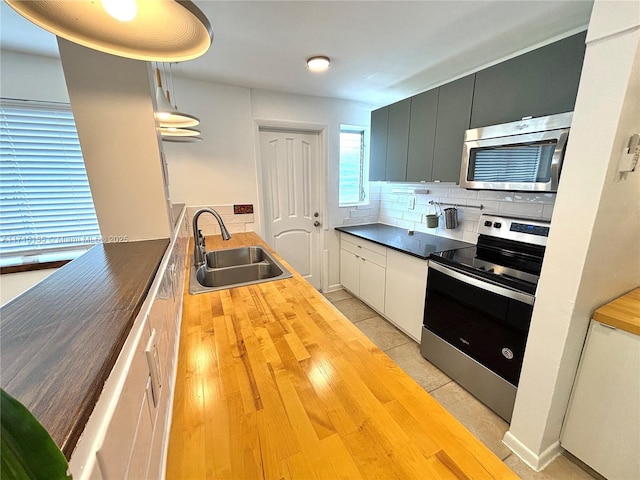 kitchen featuring decorative light fixtures, stainless steel appliances, backsplash, a sink, and butcher block countertops