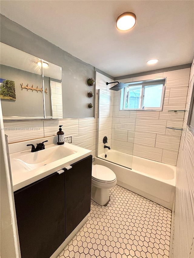 full bathroom with vanity, tile patterned floors, tiled shower / bath combo, toilet, and tile walls