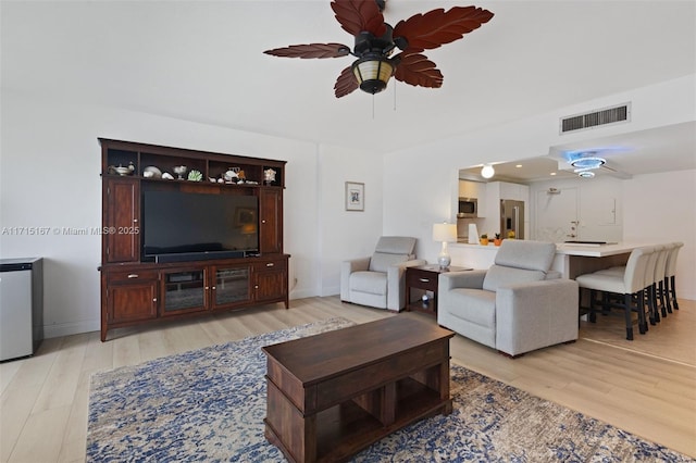 living room featuring light wood-type flooring, visible vents, ceiling fan, and baseboards