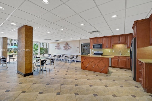 kitchen with appliances with stainless steel finishes, tasteful backsplash, a center island, light stone counters, and sink