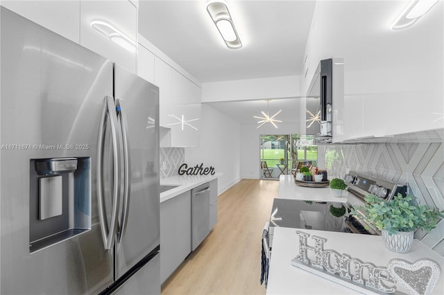 kitchen with an inviting chandelier, white cabinets, light wood-type flooring, tasteful backsplash, and stainless steel appliances