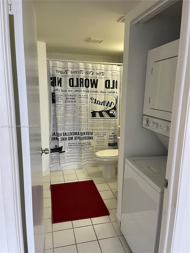 bathroom with stacked washer / dryer, tile patterned flooring, and toilet