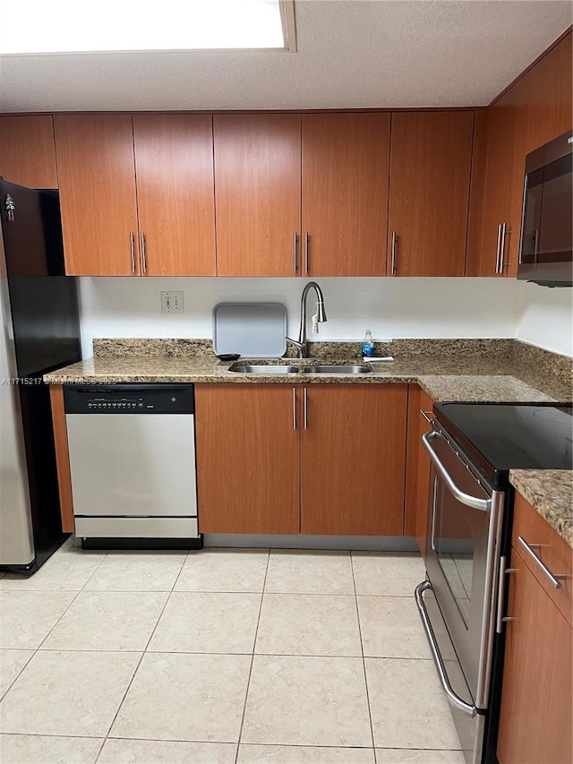 kitchen featuring sink, light tile patterned floors, dark stone counters, and appliances with stainless steel finishes