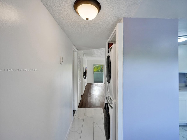 hallway featuring a textured ceiling and stacked washer and clothes dryer