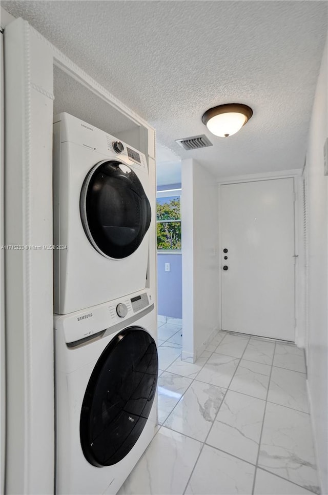 clothes washing area with a textured ceiling and stacked washing maching and dryer