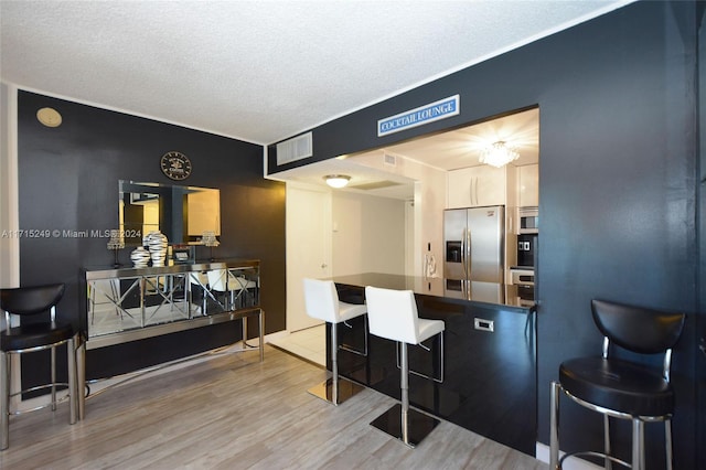 kitchen featuring kitchen peninsula, appliances with stainless steel finishes, a kitchen breakfast bar, a textured ceiling, and wood-type flooring