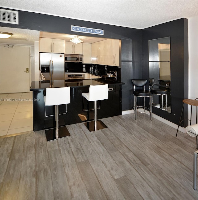 kitchen featuring hardwood / wood-style flooring, a textured ceiling, appliances with stainless steel finishes, kitchen peninsula, and a breakfast bar area